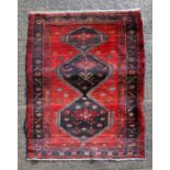 A Persian handmade woollen rug with three central medallions on a red ground, 190 by 124cms (75 by
