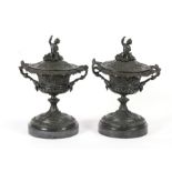 A pair of classical style bronze twin handled urns and covers, surmounted a cherub on black marble