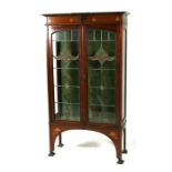 An Art Nouveau inlaid mahogany display cabinet, the pair of leaded glass doors enclosing a shelved