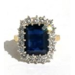 An 18ct gold sapphire and diamond cluster ring, the central emerald cut sapphire (approx 6.42ct)