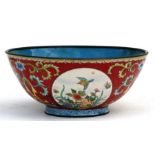 A Chinese enamel bowl decorated with birds, flowers and butterflies within roundels, on a red