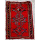 A Persian woollen handmade rug with geometric design on a red ground, 144 by 91cms (57 by 36ins).