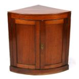 A mahogany bow fronted two-door corner cupboard, on plinth base, 74cms (29ins) wide.