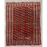 A Pakistani Bokhara hand knotted woollen rug with elephants foot motif design on a red ground, 174