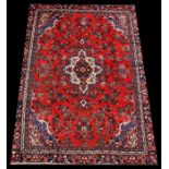 A Persian Hamadan woollen handmade rug with central medallion within foliate borders, on a red