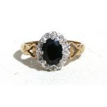 A 9ct gold oval sapphire ring surrounded by twelve small diamonds, with ornate shoulders, approx