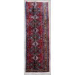 A Persian Tabriz woollen handmade runner with central medallions within a stylised border on a red