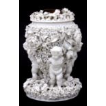 A Victorian pottery oil lamp base with three putto supporting a flower encrusted reservoir, 28cms (