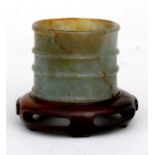 A Chinese figured jade open ended cylinder on a pierced hardwood stand, 4cms (1.5ins) high, 5cms (