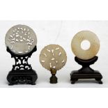 Two Chinese pierced jade discs, one on a pierced hardwood stand; together with a Chinese jade bi