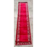A Persian Tabriz woollen hand knotted runner with stylised borders on a claret ground, 380 by