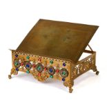 A Gothic pierced brass book stand set with glass coloured cabochons, 33cms (13ins) wide.