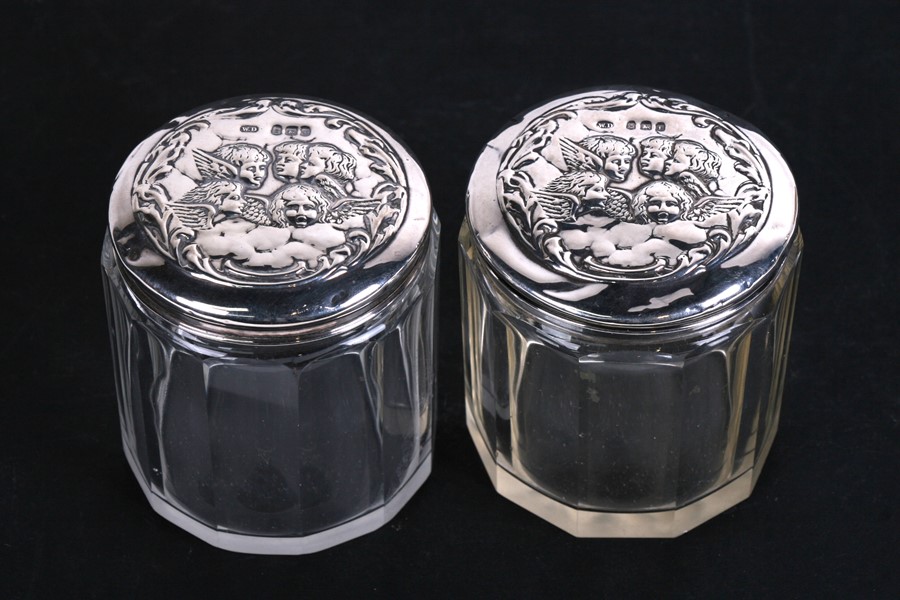 A pair of Edwardian silver topped dressing table jars embossed with cherubs, Birmingham 1905,