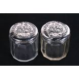 A pair of Edwardian silver topped dressing table jars embossed with cherubs, Birmingham 1905,