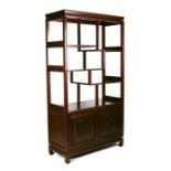 A Chinese hardwood display stand with multi level shelves above a pair of carved cupboard doors,