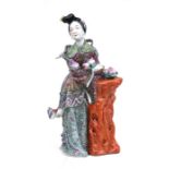 A Chinese famille rose figure in the form of a robed lady holding peaches next to a tree stump,