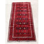A Persian Baluch woollen hand made rug with repeated guls within a stylised border, on a red ground,