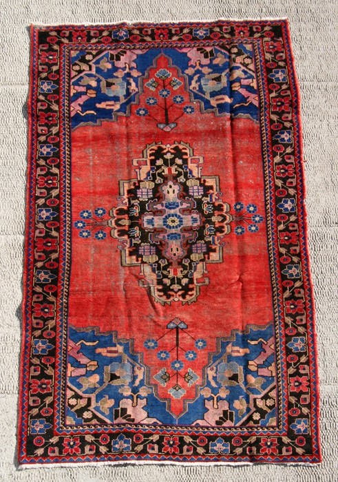 A Persian Baluch woollen hand knotted rug with stylised floral design on a red ground, 250 by 140cms