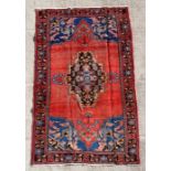 A Persian Baluch woollen hand knotted rug with stylised floral design on a red ground, 250 by 140cms