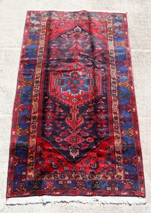 A Persian Hamadan woollen hand knotted rug with central stylised gul on a red ground, 235 by