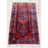 A Persian Hamadan woollen hand knotted rug with central stylised gul on a red ground, 235 by