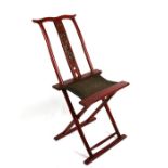 A Chinese red lacquer folding chair, the carved back splat surmounted with a pair of crossed flags.