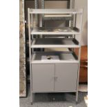 Painted grey metal storage cabinet with four open shelves, cupboard below, on circular supports,