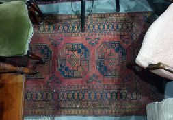 Red ground Eastern floor rug with three central elephant foot medallions, decorated in black,