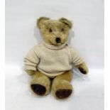 Small blonde straw stuffed bear with glass eyes and stitched eyes in a white knitted jumper,