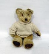 Small blonde straw stuffed bear with glass eyes and stitched eyes in a white knitted jumper,
