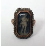 Georgian ring of shaped rectangular form, set with an enamel of a child under a glazed cover,