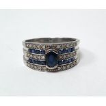 9ct white gold band ring set with a central oval mixed cut sapphire, surmounting three rows of grain