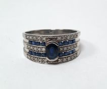 9ct white gold band ring set with a central oval mixed cut sapphire, surmounting three rows of grain