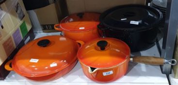 Two Le Creuset casseroles in orange, a Le Creuset orange saucepan with wood handle and a black metal