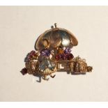 Vari-coloured gold gem set brooch modelled as a lady with a flower stall beneath a parasol, set with