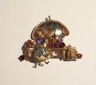 Vari-coloured gold gem set brooch modelled as a lady with a flower stall beneath a parasol, set with