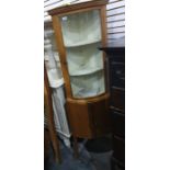 A 20th century light oak corner cabinet, the bowfront glazed door enclosing shelves, above two