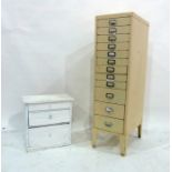 A narrow metal filing cabinet of 12 drawers in painted cream and a white painted table-top three-