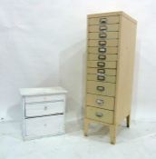 A narrow metal filing cabinet of 12 drawers in painted cream and a white painted table-top three-