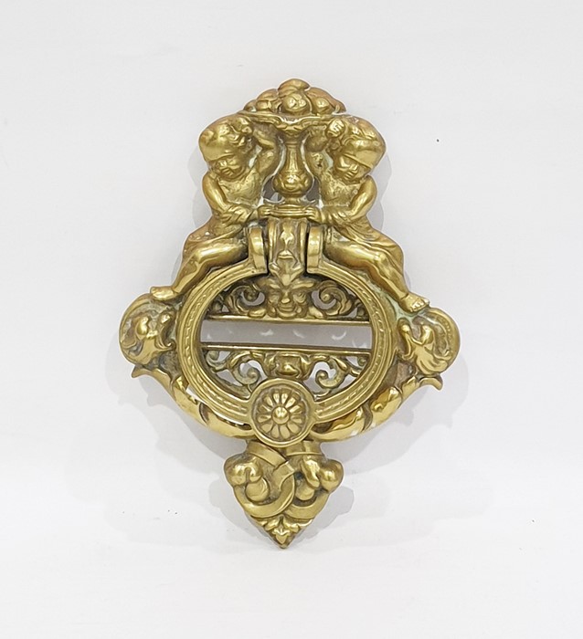 A brass door knocker cast as two putti seated above scroll work supporting a vase of fruit, the door