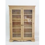 Twentieth century pine cabinet, moulded pediment above two glazed doors enclosing shelves, raised on