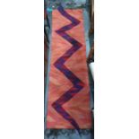 Modern runner, peach ground field sporting a ziz-zag purple, blue and red snake, the head and tail