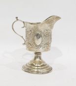 Late Victorian silver cream jug with foliate repousse decoration, on a raised circular foot,
