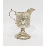 Late Victorian silver cream jug with foliate repousse decoration, on a raised circular foot,