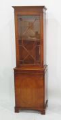 A 20th century yew narrow bookcase astragal glazed door above cupboard door to bracket feet