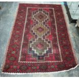 Belouch rug, red ground, central field sporting three stepped lozenge shaped repeating medallians,