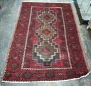 Belouch rug, red ground, central field sporting three stepped lozenge shaped repeating medallians,