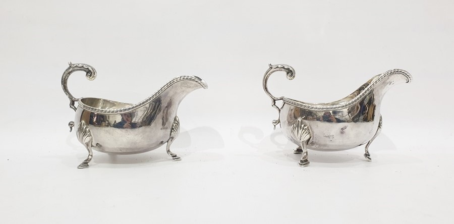 Pair of Victorian silver gravy boats with foliate scroll handles, gadrooned borders, raised on pad