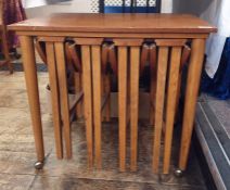 Teak coffee table with four folding coffee tables slung under, the whole on castors