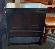 Dark elm Ercol dresser base with two cupboard doors above single drawer, turned and block supports